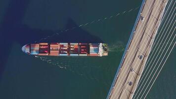 Container ship with cargo of containers passes under the bridge. Top down video