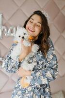 Smiling woman wearing crown holding adorable white dog with colorful fur photo