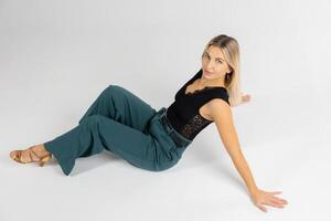 Dancer posing sitting on white floor wearing black top and green trousers photo