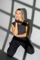 Young woman posing kneeling on the floor with window shadow projected on wall photo