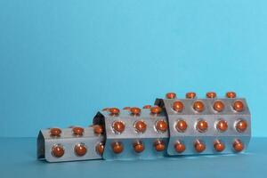 3 blister packs with separators and orange pills on blue background. Copy space for text. photo