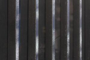 Background or texture. Metallic black fence with vertical light lines. Partically painted. photo