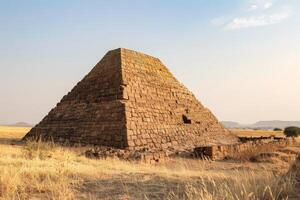 Ancient stone pyramid standing in dry grass field photo