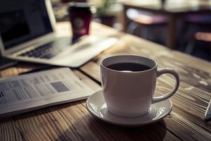 Cup of coffee waiting on a wooden table while person is working on laptop computer photo