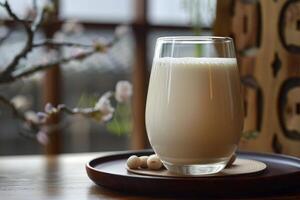 Glass of soy milk with soybeans on a wooden tray resting on a table photo