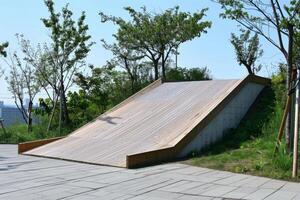 Modern wooden playground slide structure on top of hill with trees photo