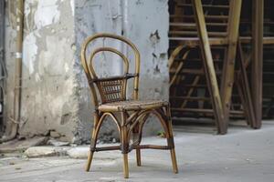 Empty rattan chair is standing on a sidewalk in front of a dilapidated building photo