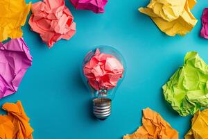Crumpled colorful paper surrounding lightbulb symbolizing ideas on blue background photo