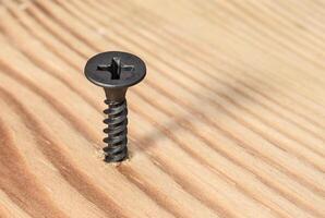 Black screw screwed into wood. Construction and repair photo