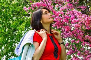 Portrait of 45 y.o. Russian woman sniffing sakura branch on background of blooming apple tree in spring. photo