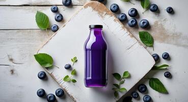 Vibrant violet blueberry juice bottle centered on white wooden board surrounded by fresh blueberries and green leaves viewed from above photo