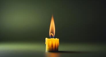 A single yellow candle flame illuminating a dark green background with space for text photo