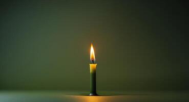 A single yellow candle flame illuminating a dark green background with space for text. photo