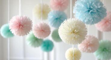 Pastel colored paper pom poms hanging from strings creating a party decoration photo