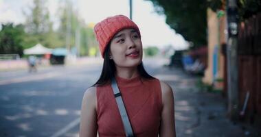 Young Asian woman leisurely strolls along a brick wall on a sidewalk in the city, happily taking photos and enjoying her surroundings. video