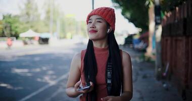 Handheld shot, Happy Asian woman smiling and enjoying mobile phone while walking on the sidewalk in the city. Enjoy the moments during journey video