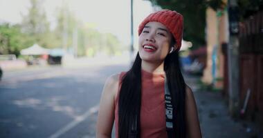 Handheld shot, Beautiful Asian woman wearing wireless headphones stands relaxed and takes a breath while looking at city street view. video