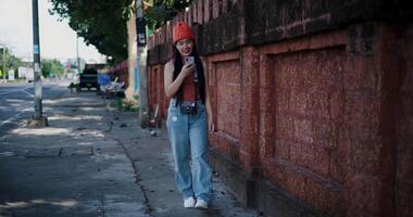 Happy Asian woman smiling and enjoying mobile phone while walking on the sidewalk in the city. Enjoy the moments during journey video