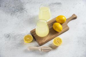 two glasses of lemonade and a wooden board with lemons photo