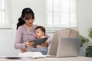 Interactive mother engaging with her baby on a tablet while managing tasks in a home office photo