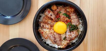 Top view of Stir fried Thai basil with crayfish and yolk egg in hot black bowl on wooden table for serving customer and eating. Flat lay of Spicy and Asian food style. photo
