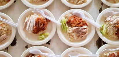 Top view or Flat lay of boiled and fried chicken with cucumber sliced, plastic spoon and fork on top rice in white plate for sale customer and serving at local street food. Asian food concept photo