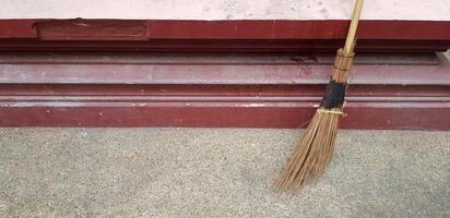 Broom Against the red wall for clean dust and sweep the garbage with left copy space. Cleaning tool and Housework concept. photo