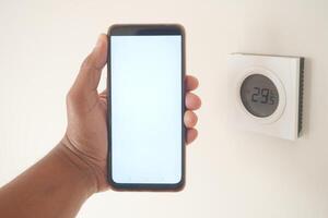 Hand Utilizing Smartphone to Interact with Digital Thermostat for Temperature Control photo