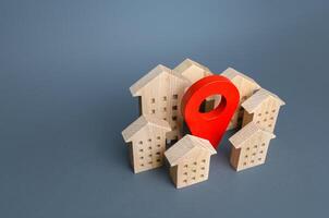 Wooden houses and a red location pin. Location, accessibility to infrastructure. Residential complex. City navigation, orienteering. Search for housing options. Moving to a different city. photo