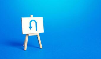 Easel with arrow turning back. Change plans, circumstances. Tactical retreat. Avoiding problems, reducing risks. Reassessment of actions. Break a promise. Return to source. Step back. Find other way. photo