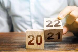 Hand flips a block changing 2021 to 2022. New year beginning. Holidays and Christmas. Trends and changes in the World. Summing work done. Build plans. New normal. Keep up with everything planned. photo