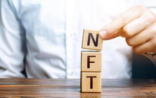 Man puts together word NFT from blocks. NFT non-fungible token. Selling digital art assets through internet auctions. Blockchain technology. Monetization, investment in cryptographic tokens photo