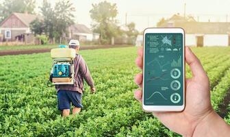 A hand with a phone on background of a farmer with agriculture smoke fog spraying machine. Crop plant care and protection from pests and fungal infection. Control of use of chemicals growing food. photo