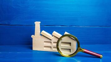 Figurine of an industrial factory plant and a magnifying glass. Big business monitoring concept, emission control. Property appraisal, enterprise audit. Compliance with sanctions policy. Analysis work photo