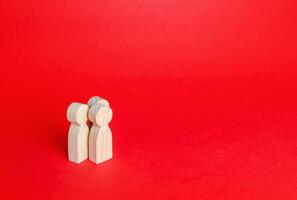 Three human figurines on a red background. Communication and discussion. Friendly relations. A meeting. Assistance, cooperation and collaboration. Place for text. photo
