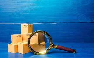 Cardboard boxes and magnifying glass. Concept of searching for goods and components. Procurement audit. Quality control. Supply and demand, distribution of products on the market. Cargo tracking photo