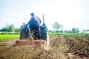 A farmer on a tractor works the soil of a farm field. Loosening surface, land cultivation. Farming, agriculture. Use of agricultural machinery and to simplify and speed up work. Plowing field. photo