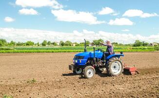 A farmer on a tractor with a mill unit crushes and processes the soil for further sowing with agricultural crops. Loosening surface, land cultivation. Plowing field. Use of agricultural machinery photo