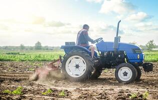 A farmer on a tractor works in the field and raises dust. Plowing field. Use of agricultural machinery and to simplify and speed up work. Loosening surface, land cultivation. Farming, agriculture. photo