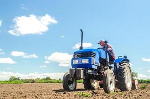 A farmer drives a tractor on a farm field. Bottom view. Loosening surface, land cultivation. Farming, agriculture. Use of agricultural machinery and to simplify and speed up work. Plowing field. photo