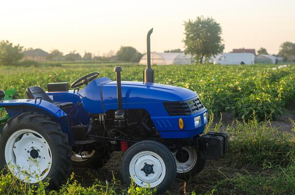 A farm tractor without a driver stands on a farm field at sunset. Subsidizing and supporting farms, modernization of technical equipment and machines. Farming and farmland. Harvest potatoes in autumn