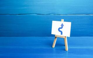 An easel with a curved arrow avoiding an obstacle. Deviation from route, side mission. Maneuvering, taking right action. Purposefulness and perseverance, confident movement towards the assigned goal. photo