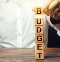 Man builds a tower of blocks with word Budget. Budgeting, forecasting income and optimizing expenses. Planning expenditure for new financial year. Saving, economy, risk assessment. Accounting audit photo