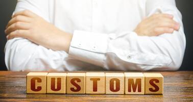 Man with folded hands on his torso and blocks with word Customs. Customs border control. Tariffs and taxes on the import of goods and products. Imports monitoring. Duties. Transportation and transit. photo