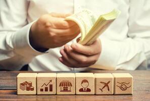 A man is counting money on the background of blocks with business attributes. Investments. Calculation of the total profit. Success, high profitability. Effective business model photo