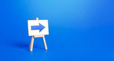 Easel with a blue right arrow. Sign of direction. Advertising of the location of a store or outlet. Minimalism. Distracting maneuver. Restriction of movement, change of course. Short road. photo
