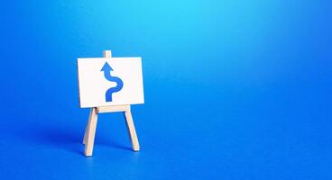 An easel with a blue arrow avoiding an obstacle. Maneuvering, taking right action. Deviation from the route, side mission. Purposefulness and perseverance, confident movement towards the assigned goal photo