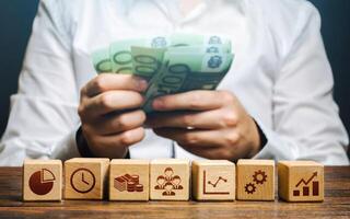 A man is counting money and blocks with business attributes. Good business model. Profitability. The rules for successful investment. High performance, great work. Company management photo
