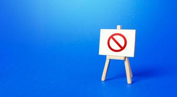 Easel with the prohibition sign NO on a blue background. Restricted area. Restrictions and Sanctions. Out of stock. Ban and Embargo. Failed strategy. Inaccessibility, taboo. Blocking. photo