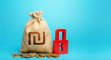Israeli shekel money bag and red padlock. Tight government control over the financial system. Blocking bank accounts and seizing assets. Cash flow monitoring. Freezing of pension savings. photo